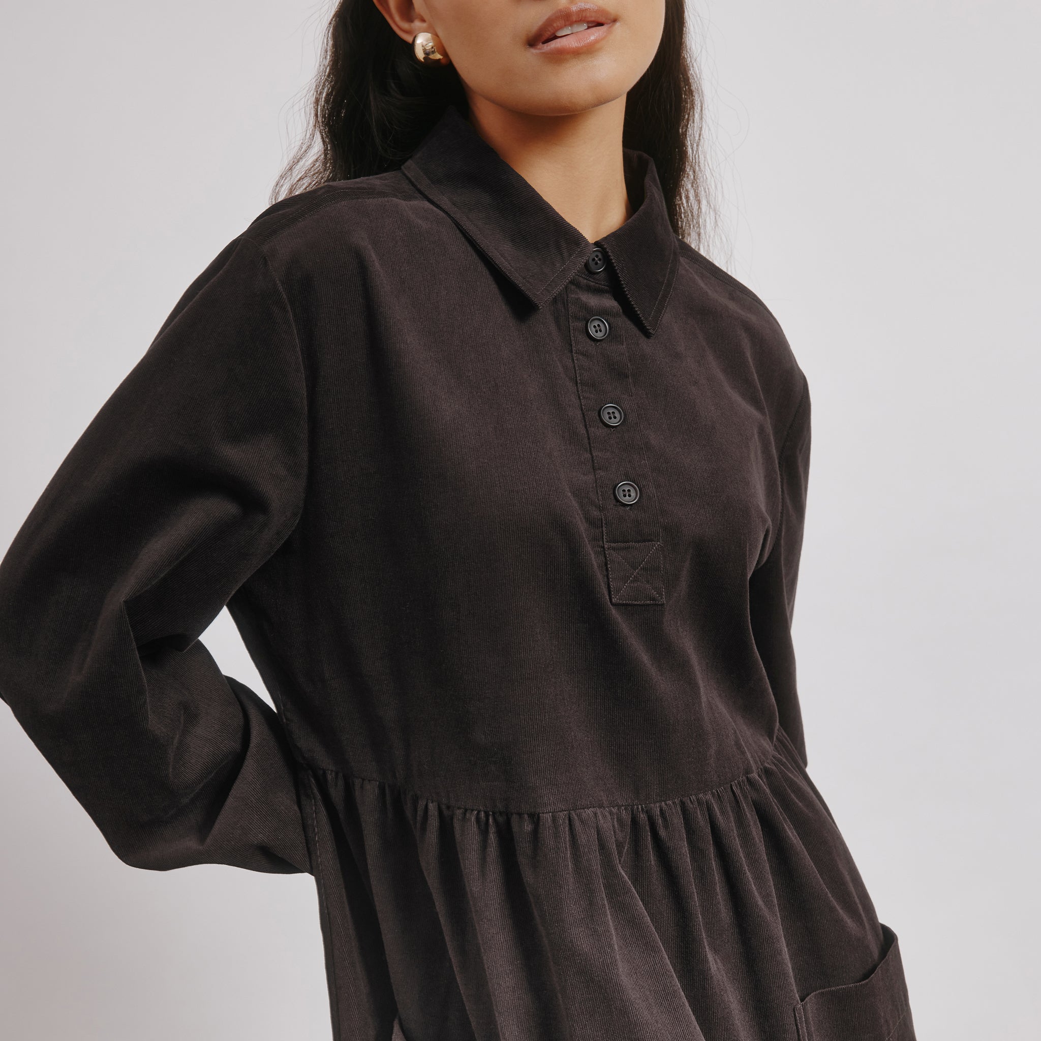 Side view of chocolate brown cord midi dress with empire waist and patch pockets.