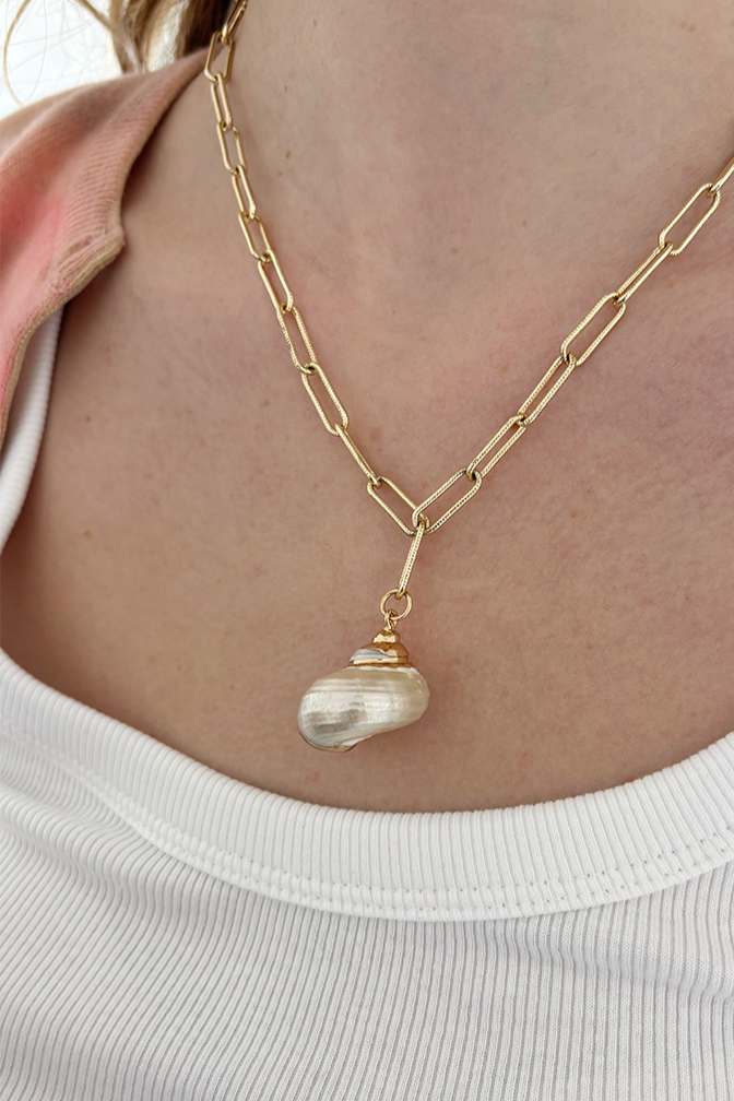 Model wearing a gold plated necklace with a shell pendant, styled elegantly.