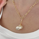 Model wearing a gold plated necklace with a shell pendant, styled elegantly.