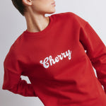 Red embroidered sweatshirt showing close-up details of embroidered logo and cherry design, soft cotton blend fabric, cozy oversized fit, perfect for casual wear and winter layering.