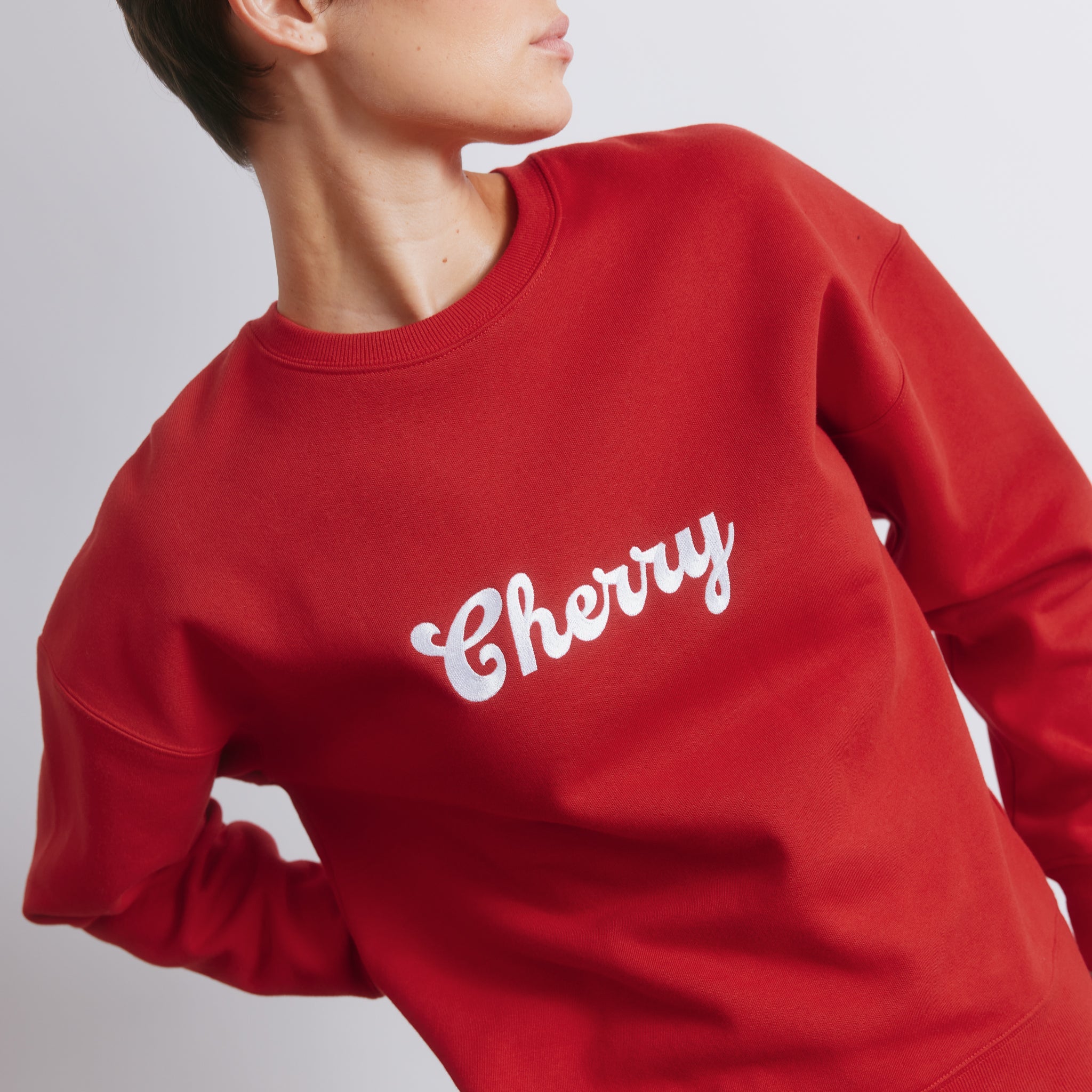 Red embroidered sweatshirt showing close-up details of embroidered logo and cherry design, soft cotton blend fabric, cozy oversized fit, perfect for casual wear and winter layering.