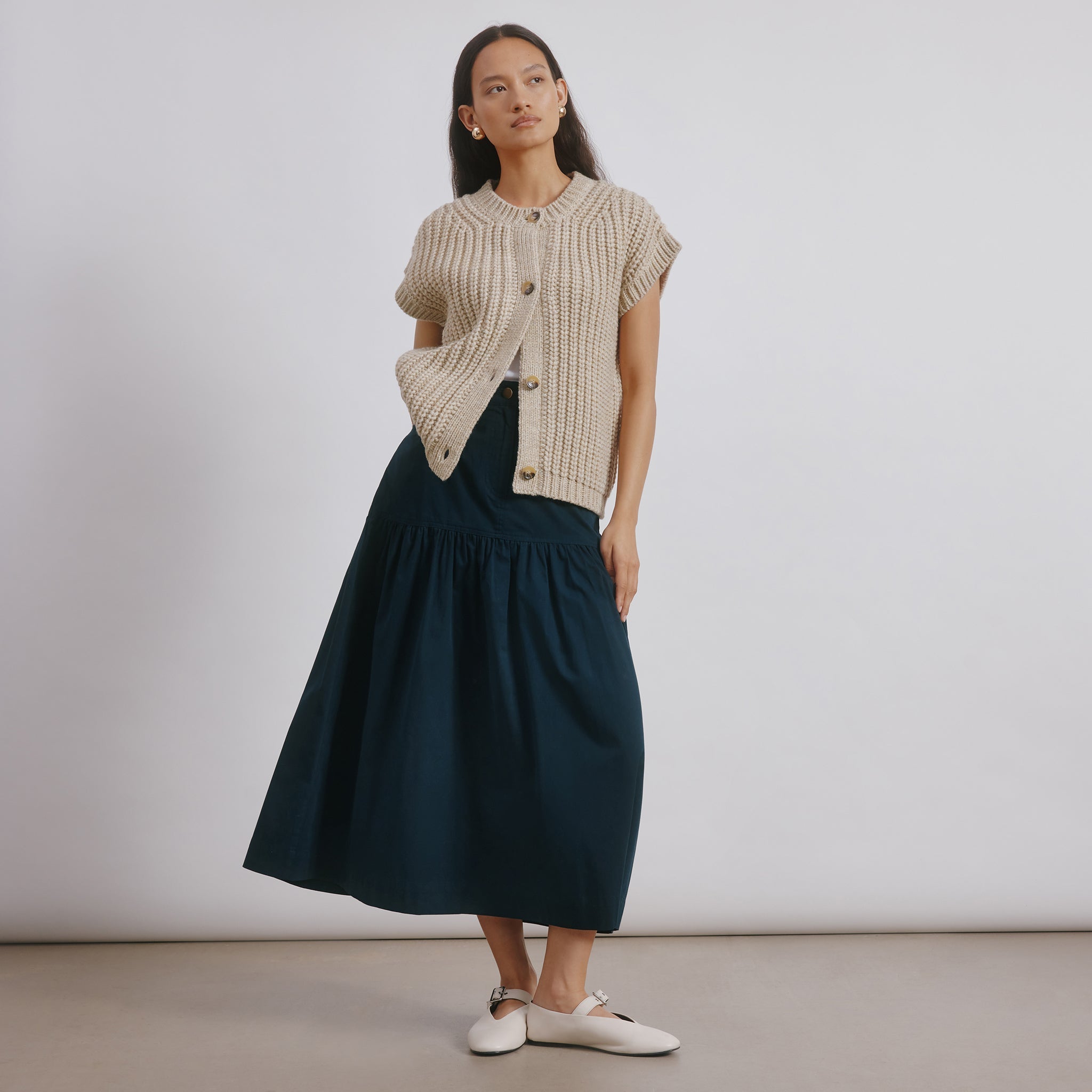 Back view of beige wool blend sleeveless cardigan vest featuring classic ribbed knit and horn buttons, an eco-friendly winter layering essential