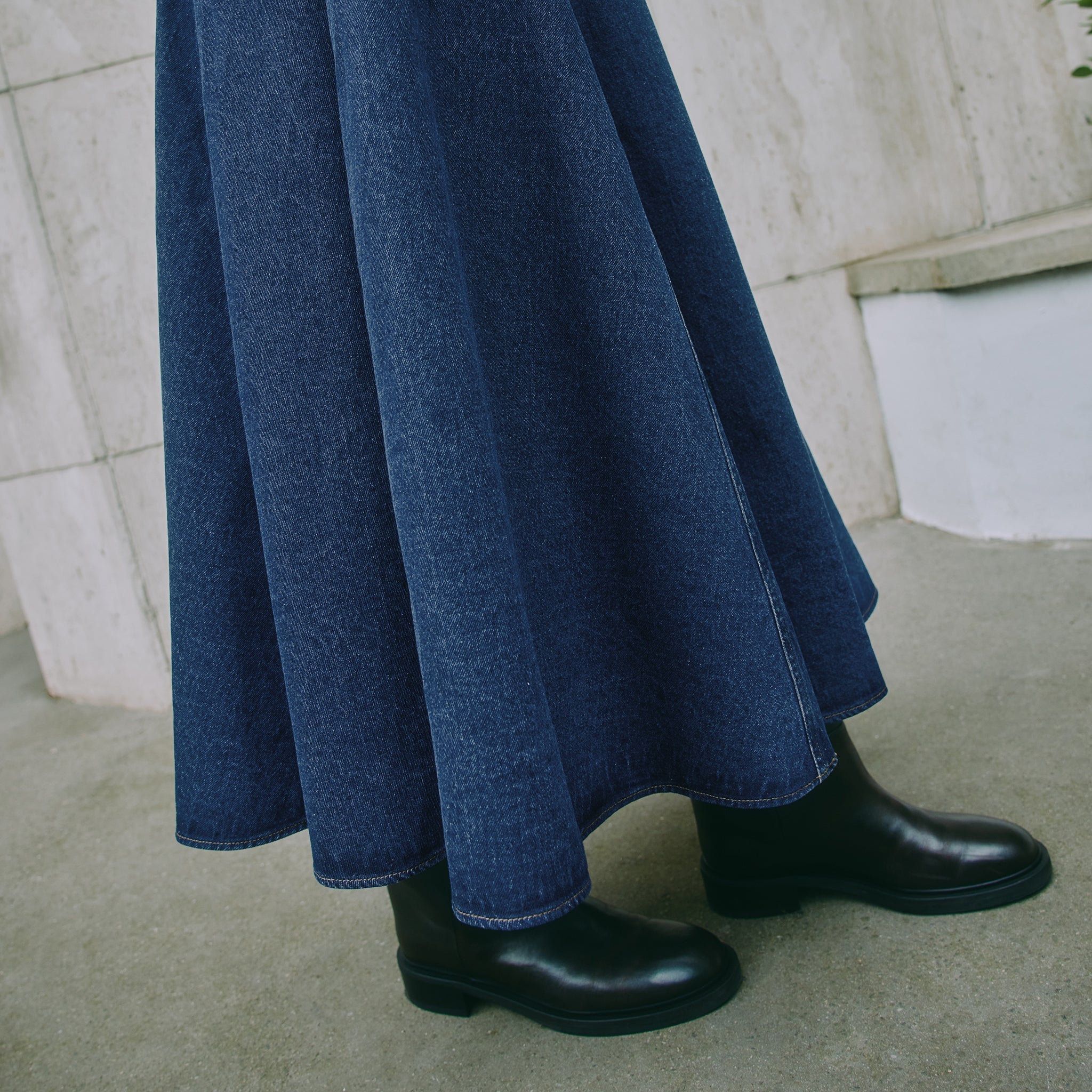 Close-up of organic cotton indigo denim skirt fabric with visible contrast stitching and basque waist design, showcasing ethical craftsmanship.