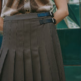 Close-up of houndstooth pleated midi skirt with faux leather buckle detail, showcasing versatile day-to-night wear and classic check design.
