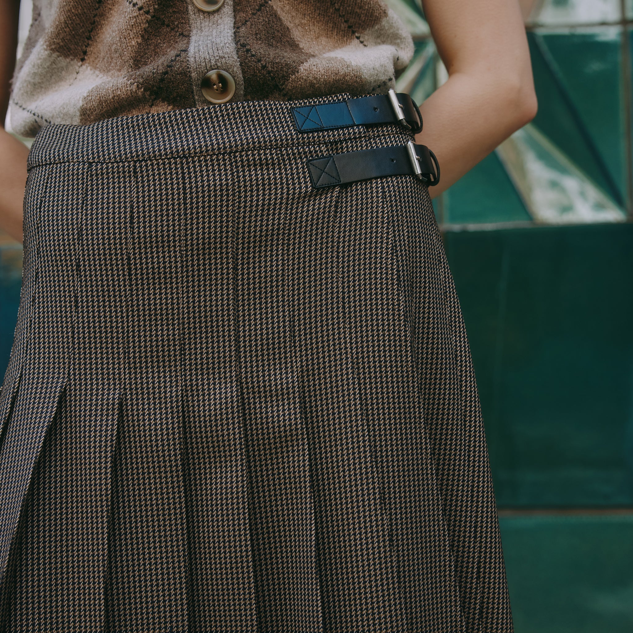 Close-up of houndstooth pleated midi skirt with faux leather buckle detail, showcasing versatile day-to-night wear and classic check design.