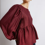 Burgundy peplum satin top styled as a textured long sleeve blouse  
