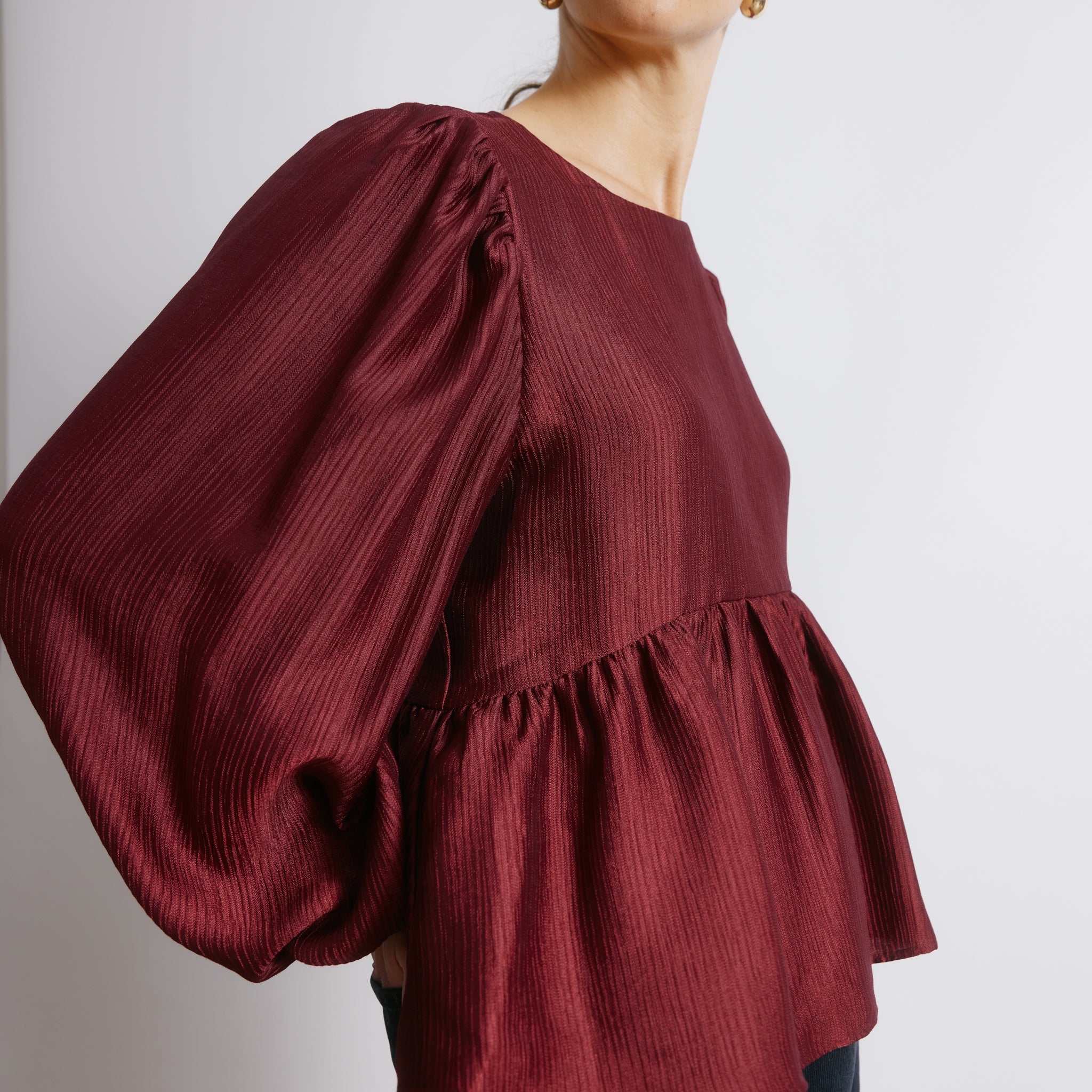 Burgundy peplum satin top styled as a textured long sleeve blouse  