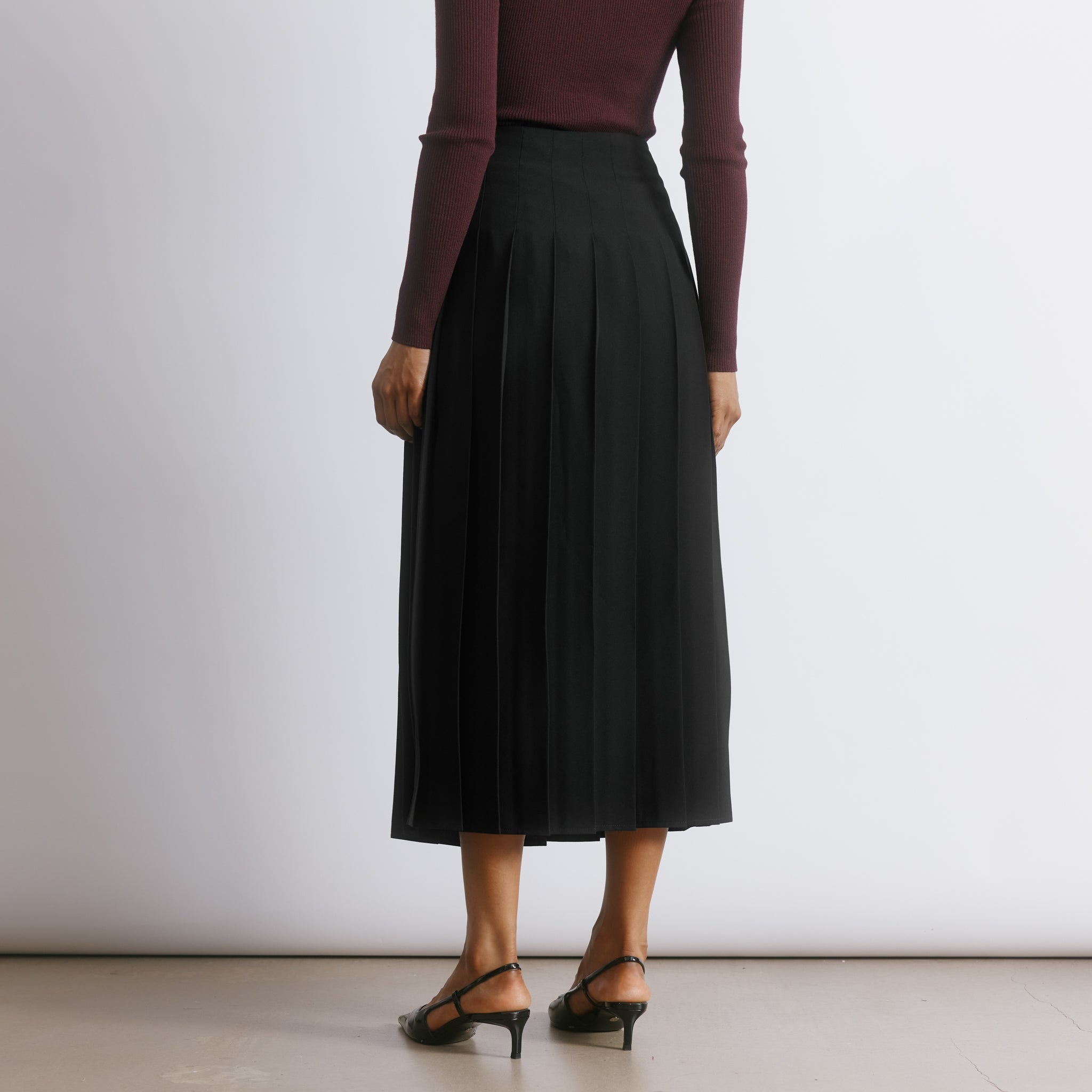Black pleated skirt made from recycled polyester with a flowing midi silhouette and elegant drape.  