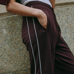 Burgundy track pants featuring athleisure style with retro stripe accents, casual drawstring waist, made from organic cotton for sustainable sportswear.