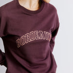 Close-up of burgundy logo on bordeaux embroidered sweatshirt, showing sustainable and ethically made cotton fabric.