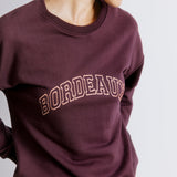 Close-up of burgundy logo on bordeaux embroidered sweatshirt, showing sustainable and ethically made cotton fabric.