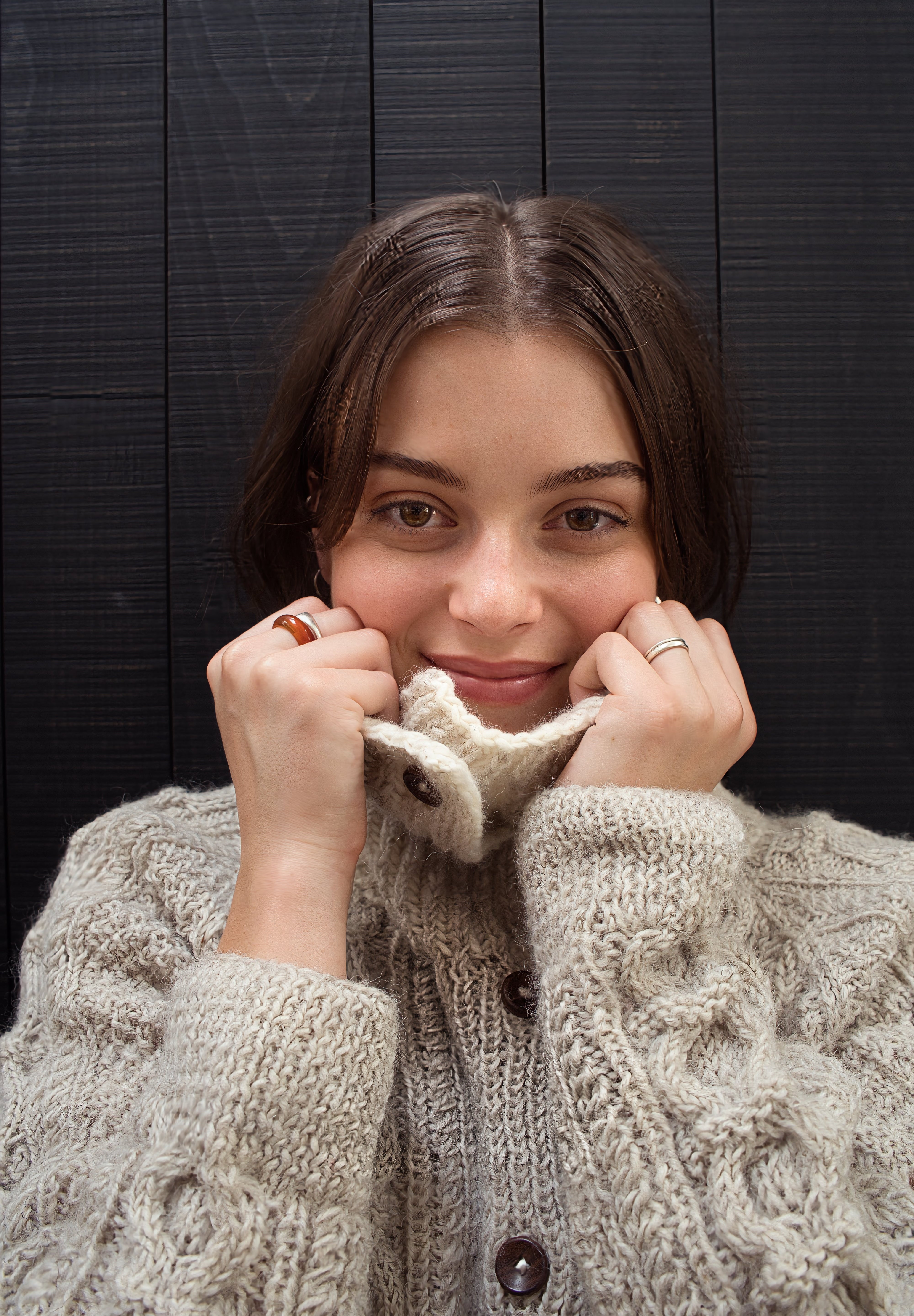 Woman wearing a beige knitted cardigan against a dark wooden background