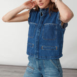 woman wearing a blue denim vest/ waistcoat with our signature white stitch detailing, two large patch pockets, and a frill collar with blue jeans against a white background