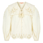 Close-up of scalloped edge on a button up white blouse with balloon sleeves and tie neck.