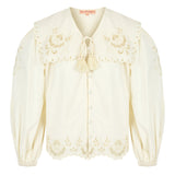 Close-up of scalloped edge on a button up white blouse with balloon sleeves and tie neck.
