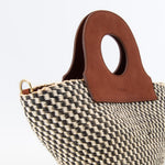 Basket bag resting on wooden surface, showcasing upcycled leather accents.