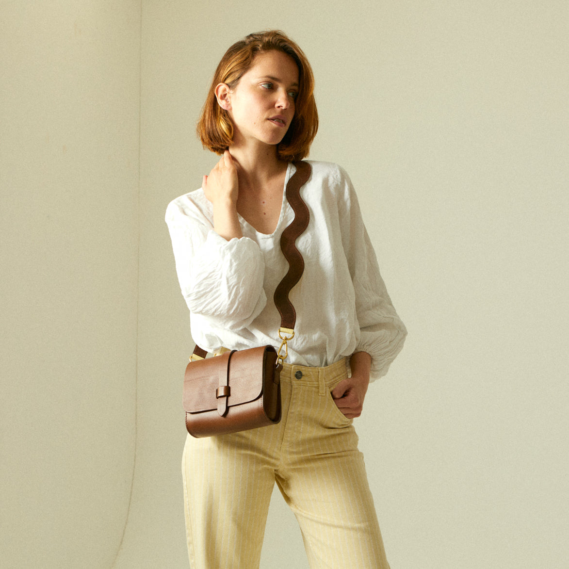Yellow leather handbag with shoulder strap on wooden chair.