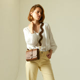 Yellow leather handbag with shoulder strap on wooden chair.