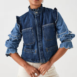 woman wearing a blue denim vest/ waistcoat with our signature white stitch detailing, two large patch pockets, and a frill collar with a blue shirt and white jeans against a white background