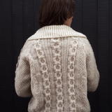 Person wearing a beige knitted cardigan with intricate patterns against a dark background