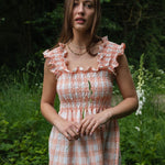 Shirred maxi dress in peach and white check pattern, featuring a smocked bodice and ruffle straps, perfect for summer.