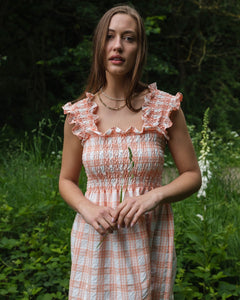 Shirred maxi dress in peach and white check pattern, featuring a smocked bodice and ruffle straps, perfect for summer.
