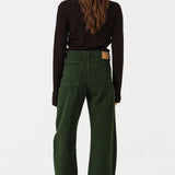 Woman wearing dark green barrel leg jeans and a brown shirt on a white background, photographed from the back