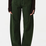 Woman wearing dark green barrel leg jeans and a brown shirt on a white background