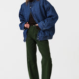 Woman wearing dark green barrel leg jeans, a brown shirt, and a dark blue houndstooth bomber jacket on a white background
