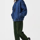 Woman wearing dark green barrel leg jeans, a brown shirt, and a dark blue houndstooth bomber jacket on a white background