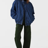 Woman wearing dark green barrel leg jeans, a brown shirt, and a dark blue houndstooth bomber jacket on a white background