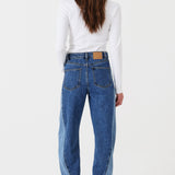 Woman wearing two toned blue barrel leg jeans and a white shirt on a white background