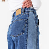 Side detail of woman wearing two toned blue barrel leg jeans and a white shirt on a white background