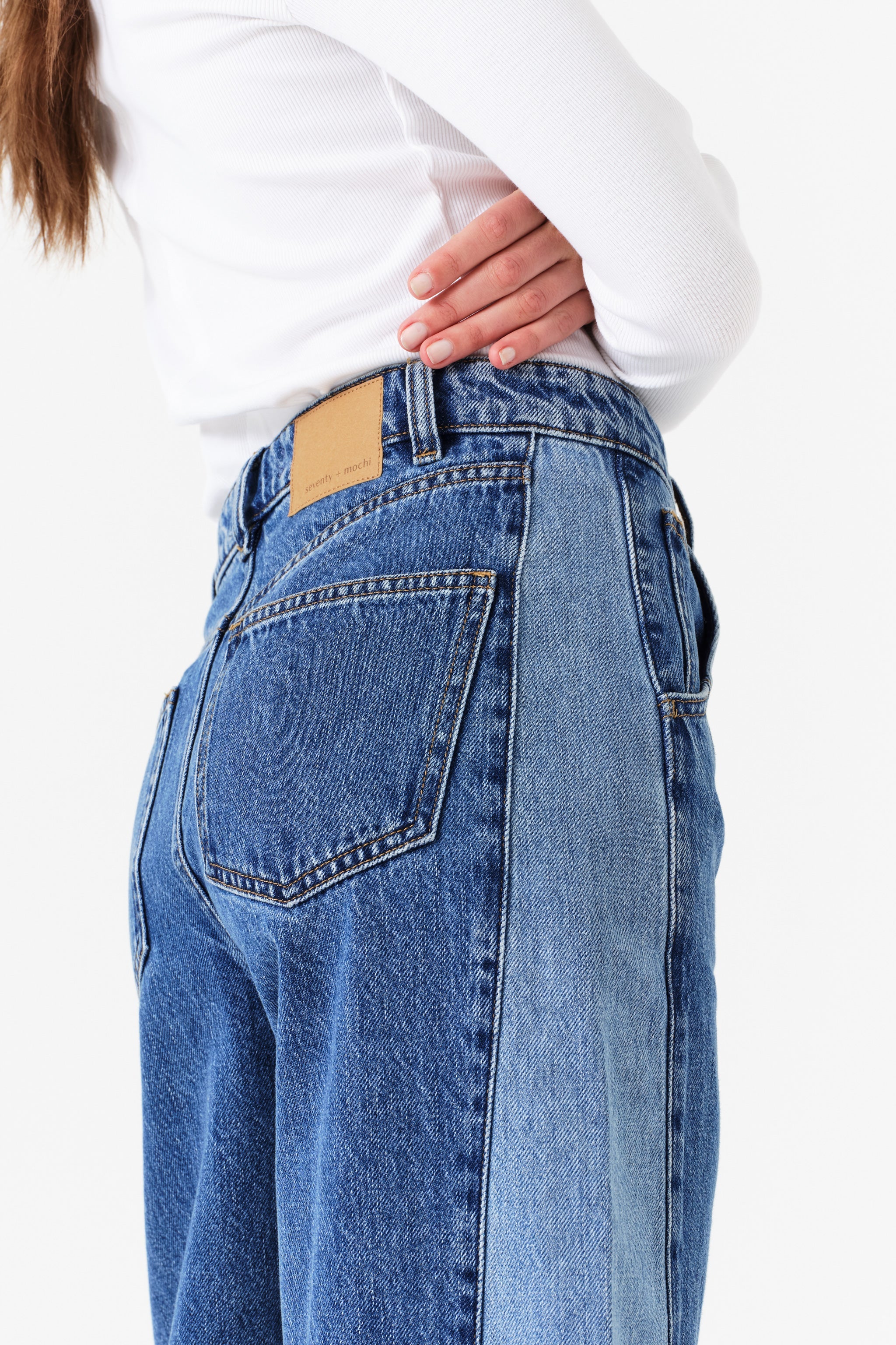 Side detail of woman wearing two toned blue barrel leg jeans and a white shirt on a white background