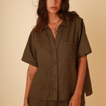 Woman wearing a short sleeve linen button down shirt with matching high waisted linen shorts.