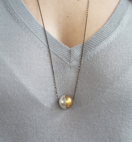 A statement necklace with two solid half-spheres creating a unified ball or two halves on the same chain, by Percy Langley