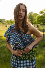 This cool blue gingham embroidered Moreena dress is by Conditions Apply. The dress is a classic one shoulder midi length in a crisp plaid print developed using light skin friendly cotton fabric that would be suitable for any day in the sun.  The beautifully embroidered frog motif adds a fun quirky twist to the statement dress